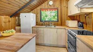 A compact kitchen with wooden walls, a built-in refrigerator, a sink, a microwave, a kettle, and a stove. - 3 bedroom awesome home in Hadsund (Hadsund)