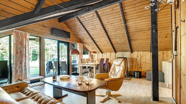 A spacious room with a high ceiling, wooden beams, a large dining table, leather seating, and a view through large windows. - 3 bedroom awesome home in Hadsund (Hadsund)