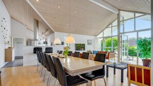Un comedor amplio con una larga mesa de madera, sillas negras y una cocina moderna al fondo.