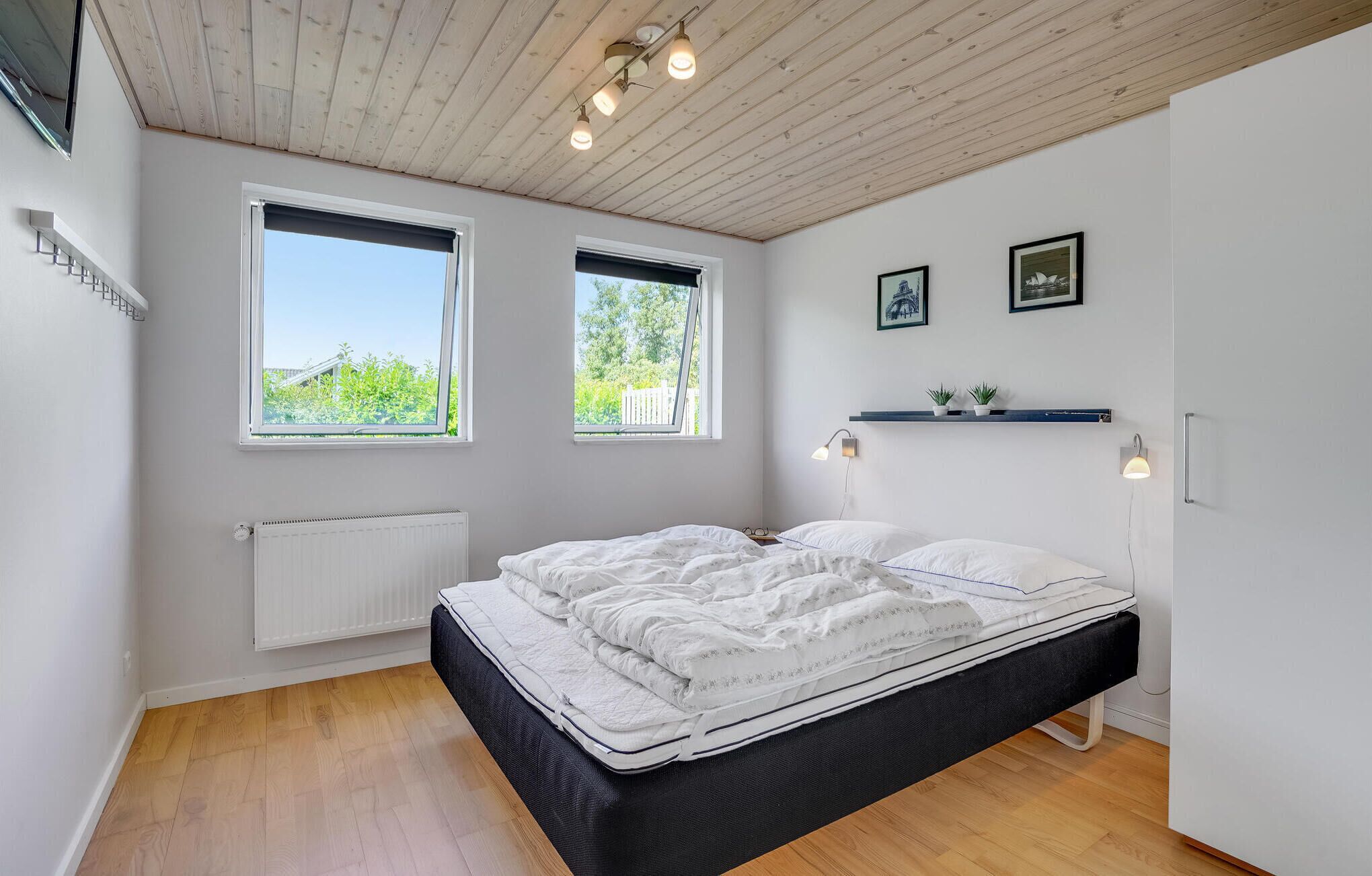 A modern bedroom with a bed, two windows, a radiator, and a shelf with plants.