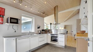 Una cocina moderna con armarios blancos, electrodomésticos de acero inoxidable, un ventanal grande y un techo alto con vigas a la vista.