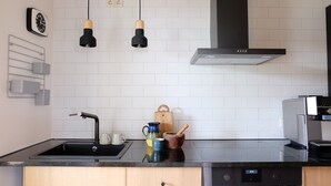 A modern kitchen with a black countertop, stainless steel appliances, a wooden cabinet, and a hanging light fixture. - designed by Mark Pohl - winner of "Best of Interior" Award 2017 (Friedrichswalde)