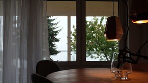 A dining area with a table, chairs, a glass candle holder, and a view of trees and water through large windows. - designed by Mark Pohl - winner of "Best of Interior" Award 2017 (Friedrichswalde)
