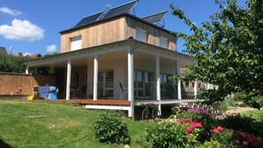 A two-story house with a wooden exterior, a covered porch, and solar panels on the roof. - designed by Mark Pohl - winner of "Best of Interior" Award 2017 (Friedrichswalde)