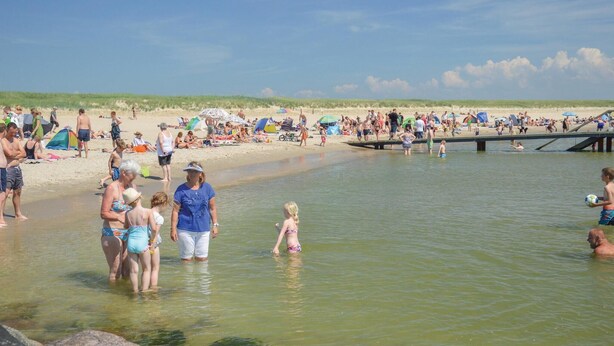 Ein voller Strand mit Menschen im Wasser und am Sand.