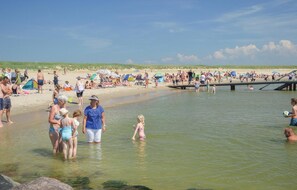 En overfyldt strand med folk i vandet og på sandet.