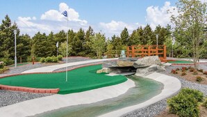 Ein Minigolfplatz mit einem grünen Putting-Bereich, einer Wasserstelle und einer Holzbrücke.