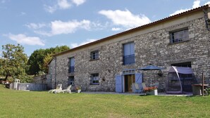 Un bâtiment en pierre avec un toit en tuiles, un patio couvert doté de sièges extérieurs et une pelouse verdoyante.