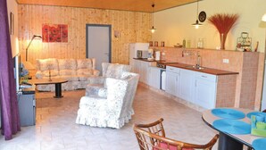 Un salon chaleureux avec un canapé et des fauteuils, un coin repas avec une table et des chaises, et une cuisine dotée de meubles blancs et d’un dosseret carrelé.