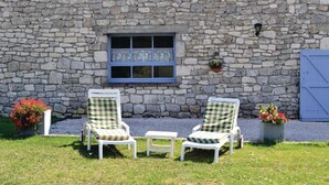 Un bâtiment en pierre avec une fenêtre, deux chaises blanches dotées de coussins à carreaux et une porte bleue.