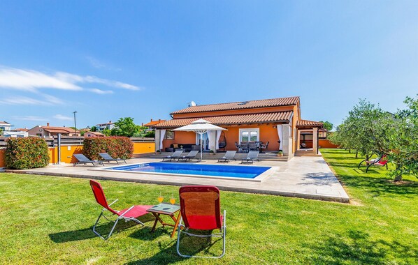Ein Haus mit Swimmingpool, Sitzgelegenheiten im Freien und einem gepflegten Rasen.