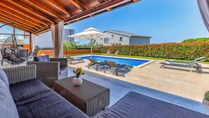 A covered outdoor area with wicker furniture, a pool, and a view of a modern house. - Pet friendly home in Skatari (Skatari)