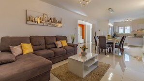 A modern living room with a brown sofa, a white coffee table, and a dining area with chairs and a table. - Pet friendly home in Skatari (Skatari)