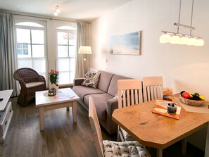 Un salon moderne avec un canapé, une table à manger, un fauteuil en osier, une lampe et un tableau accroché au mur.
