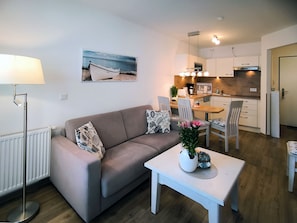 A modern living room with a sofa, a coffee table, and a dining area with chairs and a table. - Haus Meeresblick FeWo Albatros A 2.33 Ref. 243476 - FeWo Albatros A 2.33 Ref. (Baabe)