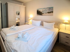 A double bed with white linens, two bedside lamps, a painting of a beach scene, and a wardrobe. - Haus Meeresblick FeWo Albatros A 2.33 Ref. 243476 - FeWo Albatros A 2.33 Ref. (Baabe)