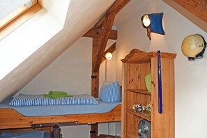 Un dormitorio tipo loft con techo inclinado, vigas de madera, una cama litera, un estante pequeño con objetos decorativos y un globo terráqueo colgado en la pared.
