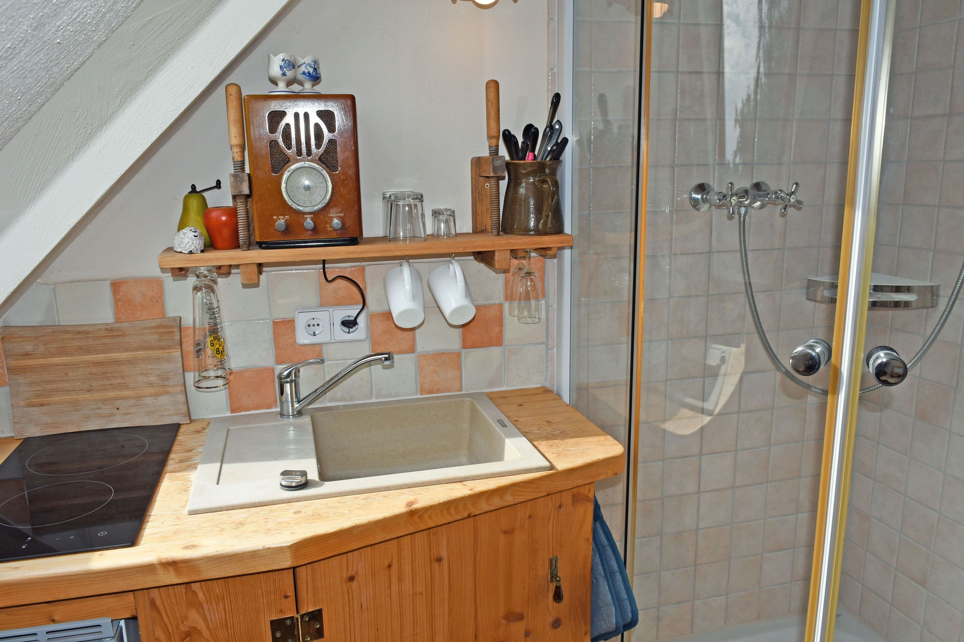 Una cocina con encimera de madera, un fregadero y una estufa empotrada. Encima del fregadero hay una repisa con diversos utensilios de cocina.