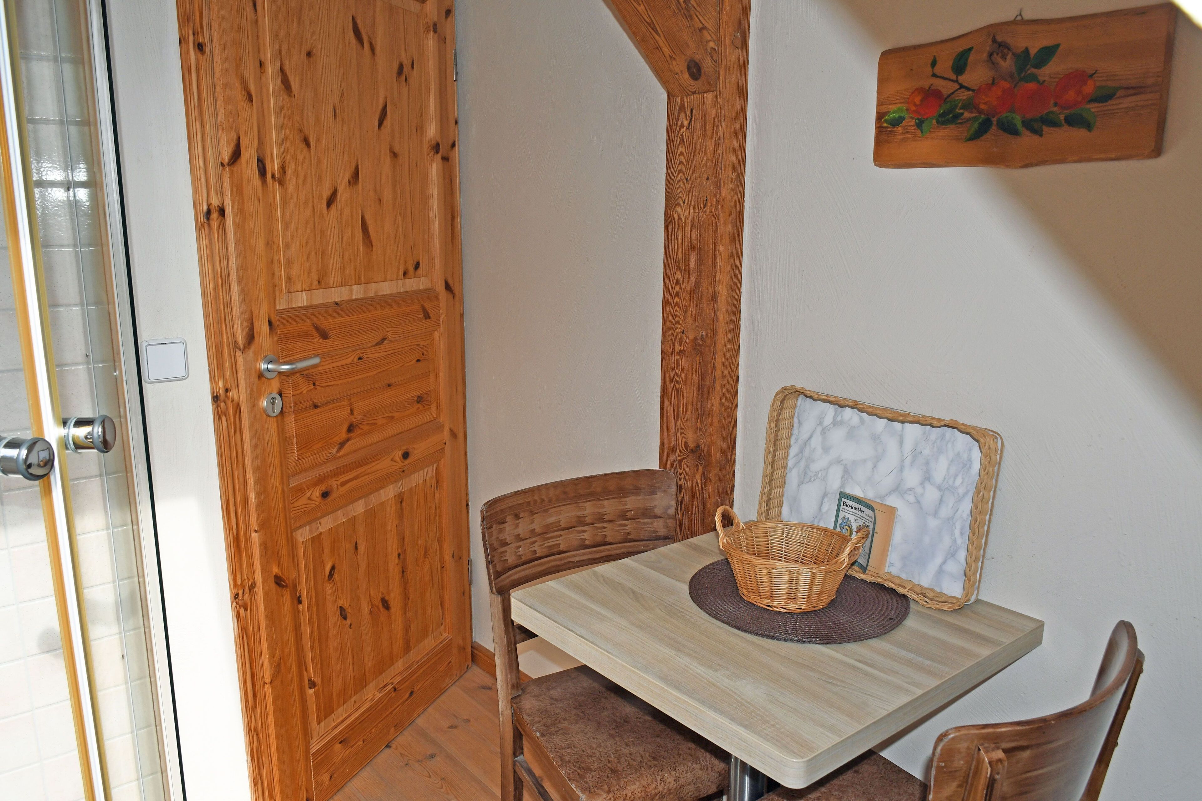 A wooden door, a small table with a basket, and a mirror on the wall.
