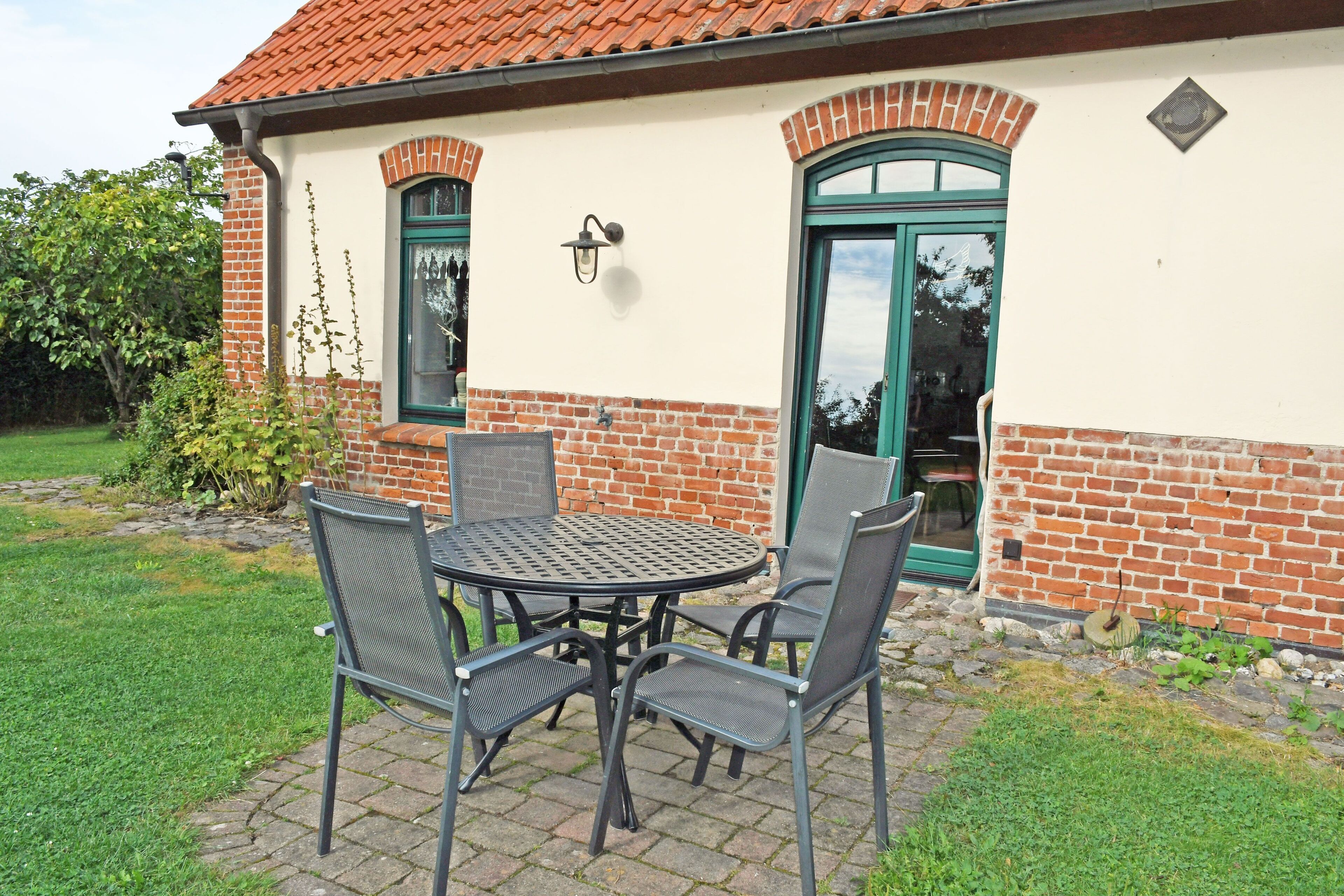 Eine Terrasse im Freien mit einem runden Tisch, vier Stühlen, einer Ziegelwand und einer grünen Tür.