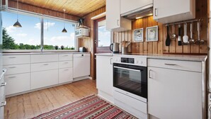 Una cocina moderna con armarios de madera, horno empotrado y un amplio ventanal con vistas a la vegetación.