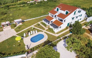 Un edificio grande de color blanco con techo rojo, varios balcones y una piscina.
