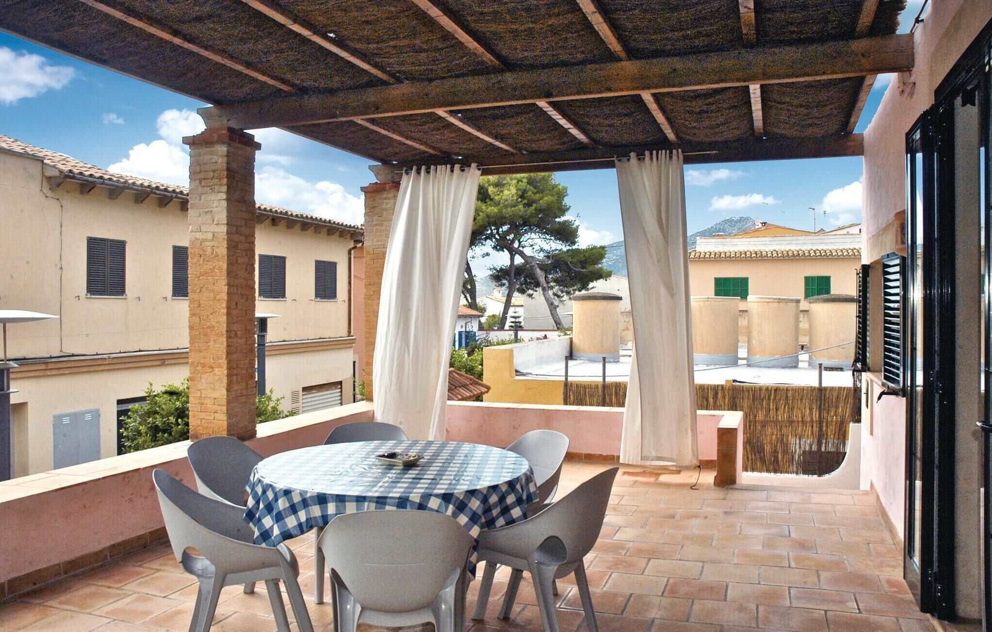 Un patio techado al aire libre con una mesa redonda y sillas, con vista a una zona residencial con edificios y un árbol.