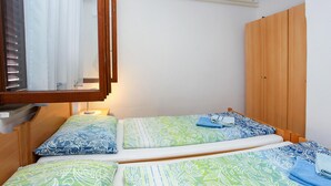 A small, single-bed room with a wooden wardrobe, a window with curtains, and a bedside table with a lamp. - Beach front apartment in Lucija with WiFi (Lucija)