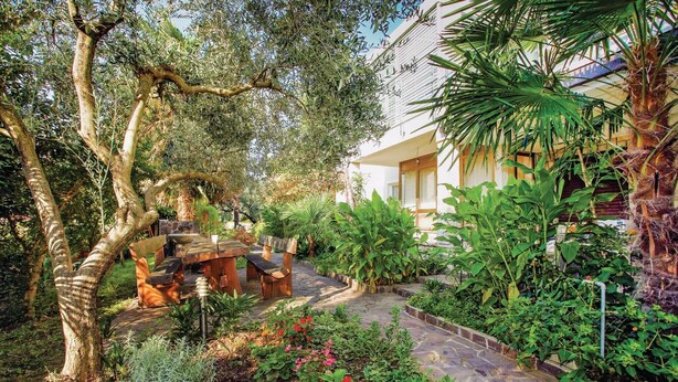 A garden with a stone pathway, wooden furniture, and various plants. - Beach front apartment in Lucija with WiFi (Lucija)