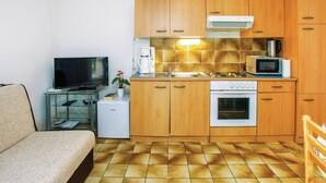 A compact kitchen with wooden cabinets, a built-in oven, a microwave, and a small refrigerator. - Beach front apartment in Lucija with WiFi (Lucija)