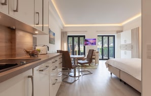 A modern hotel room with a kitchenette, a dining area, and a bed.