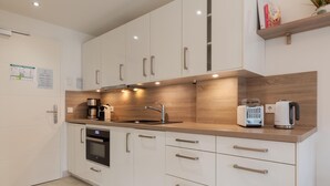 Eine moderne Küche mit weißen Schränken, einer Holz Arbeitsplatte, einem eingebauten Backofen, einer Kaffeemaschine, einem Toaster und einem Wasserkocher.