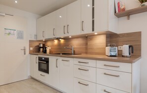 A modern kitchen with white cabinetry, a wooden countertop, a built-in oven, a coffee maker, a toaster, and a kettle. - Beach front apartment in Binz with WiFi (Prora/Rügen)