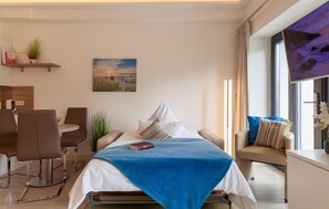 Une chambre d’hôtel moderne équipée d’un lit, d’un coin repas, d’un canapé et d’une grande fenêtre donnant sur un paysage agréable.