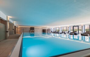 A large indoor swimming pool with a fireplace, sun loungers, and a view of the outdoors.