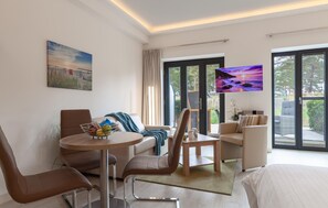 Ein modernes Hotelzimmer mit Sofa, Stühlen, Esstisch und Fernseher.