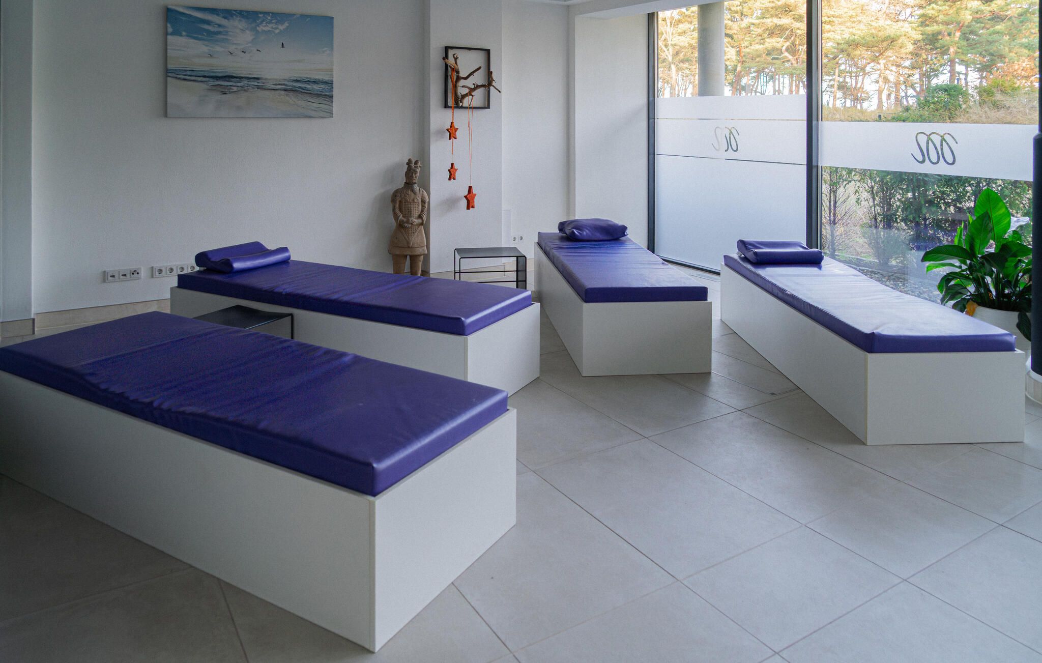 A modern spa room with three treatment beds, a small statue, and a painting on the wall.
