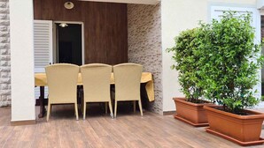 An outdoor patio with a table and chairs, a potted plant, and a door leading to a covered area. - Holiday apartment with garden terrace near the beach Špadići Poreč (Poreč)