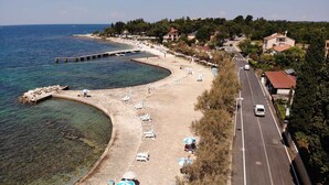 A coastal road with beachside amenities, including sun loungers and umbrellas, and a pier extending into the sea. - Holiday apartment with garden terrace near the beach Špadići Poreč (Poreč)