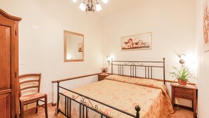 A bedroom with a bed, a wooden chair, a nightstand, a mirror, and a chandelier. - Stunning home in Orentano PI (Orentano PI)
