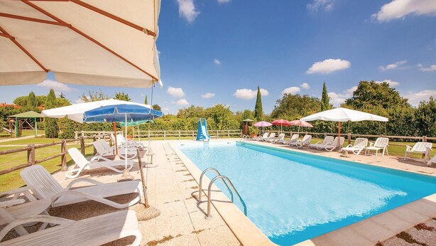 A swimming pool with lounge chairs and umbrellas, surrounded by greenery and trees. - Stunning home in Orentano PI (Orentano PI)