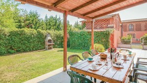 An outdoor patio with a wooden table set for dining, surrounded by chairs. A brick oven is visible in the background. - Stunning home in Orentano PI (Orentano PI)