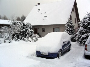 Ein Wohngebäude mit verschneitem Dach und geparkten Autos.