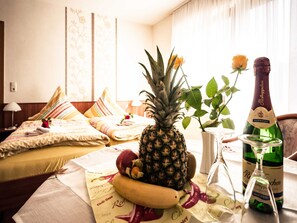 Ein Hotelzimmer mit einem Bett, Obst auf einem Tisch, einer Champagnerflasche und einer Topfpflanze.