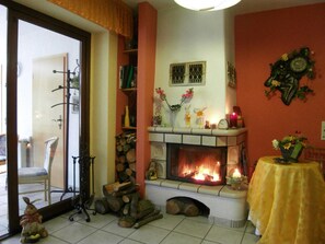 Ein gemütliches Wohnzimmer mit Kamin, einem Sessel, einem Tisch mit einer Vase und einer Wanduhr.