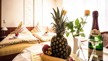 Ein Hotelzimmer mit einem Bett, Obst auf einem Tisch, einer Champagnerflasche und einer Topfpflanze.