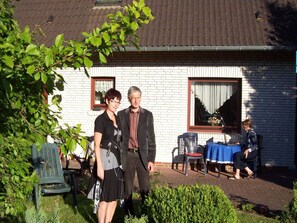 Ein Backsteinhaus mit einem Ziegeldach, ein Fenster mit Vorhang und ein Tisch mit Stühlen vor der Tür.