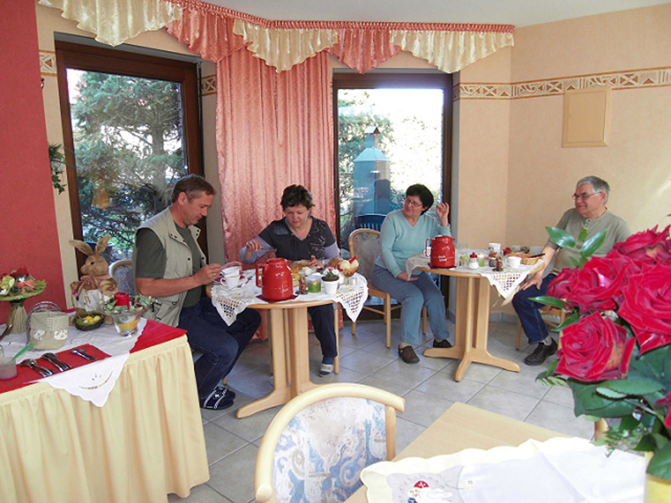 Un comedor con una mesa dispuesta para cuatro personas, una silla con estampado floral y un jarrón con flores rojas.