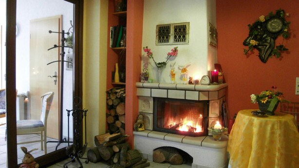 A cozy living room with a fireplace, a chair, a table with a vase, and a clock on the wall. - Vacation apartment 1 - Family-run guesthouse & vacation apartments Fischer-Haus (Trassenheide)