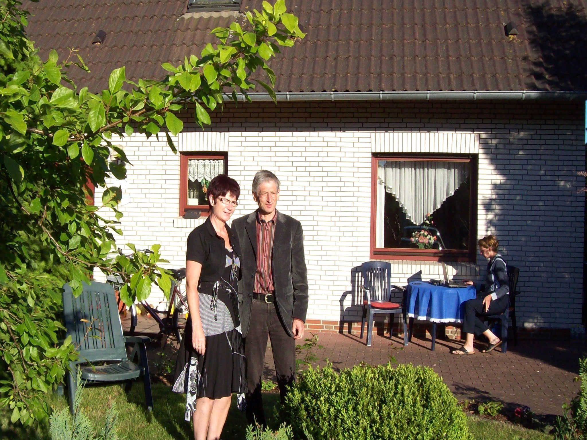 Ein Backsteinhaus mit einem Ziegeldach, ein Fenster mit Vorhang und ein Tisch mit Stühlen vor der Tür.